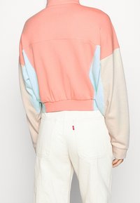 Färgglad sweatshirt med en korallfärgad ovandel, ljusblå och beige sidopaneler, ribbad nederkant och hög krage. Mjuk textur.