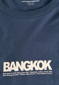 Μπλε μπλουζάκι Jack & Jones Originals με τη λέξη "BANGKOK" με έντονα λευκά γράμματα και ονόματα περιοχών της Μπανγκόκ από κάτω στα αγγλικά και στην ταϊλανδική γραφή.