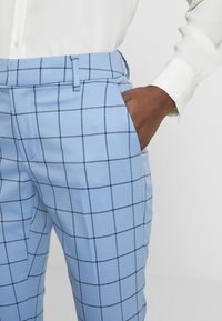 Light blue plaid trousers featuring a grid pattern in dark blue, made of textured fabric with side pockets and a tailored fit.