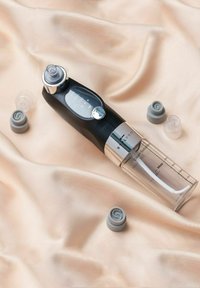 Appareil facial en plastique noir et transparent avec des accents argentés, doté d'un panneau de contrôle et de pointes en silicone grises interchangeables, sur un tissu beige doux.