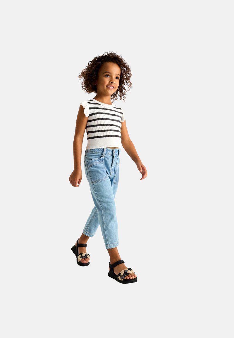 Top corto a righe bianche e nere con maniche a volant, abbinato a jeans a vita alta azzurri e sandali neri intrecciati.