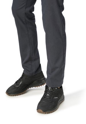 Zapatillas deportivas negras con una superficie texturada, que presentan un diseño con cordones y una suela de goma gruesa y con taco, combinadas con pantalones azul oscuro.