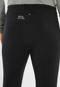 Leggings sportivi neri presentano un design elegante, una texture liscia e una piccola tasca con zip con una grafica montana sopra di essa.