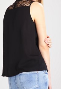 Haut noir sans manches présentant un empiècement en dentelle, un tissu doux, un ourlet arrondi et une coupe décontractée, associé à un jean en denim bleu clair.