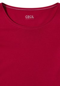 Czerwona bluzka z krótkim rękawem, wykonana z miękkiego materiału, z okrągłym dekoltem. Logo marki "CECIL" jest nadrukowane na białym tle przy kołnierzu.