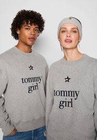 Felpe grigie con ricamo "tommy girl" e accenti a forma di stella. Un cerchietto grigio abbinato su una persona completa l'outfit.