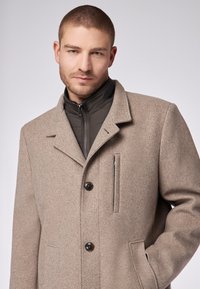 Hellbrauner Wollmischmantel mit Reverskragen, einem Reißverschluss-Innenfutter und Knopfverschluss. Verfügt über Taschen vorne und eine glatte Textur.