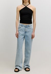 Zwarte geribbelde haltertop met een diagonale kruisband, gecombineerd met lichtblauwe wijde jeans en zwarte platte sandalen. Glad textuur is opvallend.