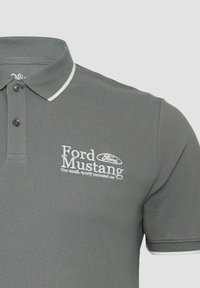 Grijze polo met witte bies op de kraag en mouwen, geborduurd "Ford Mustang" logo en tekst op de linkerborst.
