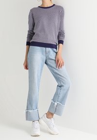 Svetr v námořnické modři a bílé s potiskem, s žebrovanými manžetami, ve spojení se světle modrými džínami s oděrkami a bílými teniskami. Neformální outfit s kontrastními detaily.