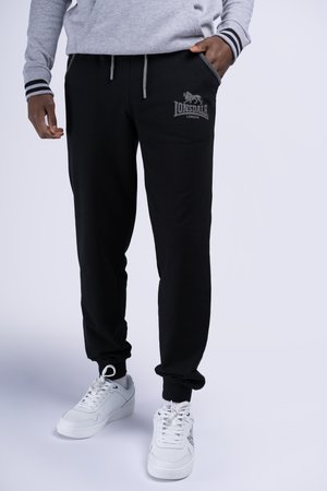 Zwarte sweatpants met een trekkoord, zijzakken en een Lonsdale-logo op de linkerdij. Gecombineerd met witte sneakers.