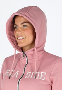 Felpa con cappuccio rosa chiaro con chiusura a zip e cordini. "SEA SIDE" ricamato in bianco sulla parte anteriore. Tessuto liscio.