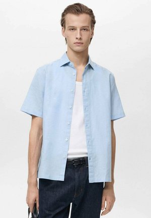 Camicia azzurro chiaro a maniche corte realizzata in un tessuto leggero, con una chiusura a bottoni sul davanti, abbinata a una canotta bianca e a jeans scuri.