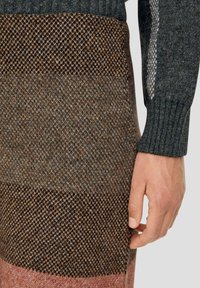 Stickad tröja med en ribbad mörkgrå krage, ett texturerat mönster i bruna och rosa ränder, samt en åtsmitande manschett runt handleden.