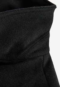 Schwarzer Fleece-Stoff mit weicher Textur und einem gefalteten, gestuften Design. Sichtbare Nähte und ein glattes Nahtdetail heben die gesamte Struktur hervor.