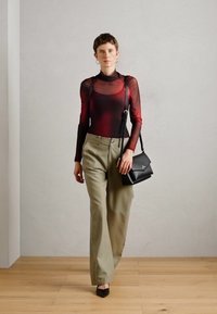 Haut rouge et noir transparent à manches longues, col montant, associé à un pantalon ample vert olive. Tient un petit sac à main noir. Ballerines pointues classiques.