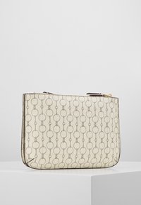 Beige rektangulär clutch med upprepande kedjemönster, svarta detaljer och dragkedjestängning, visad på en vit pelare mot en enkel bakgrund.