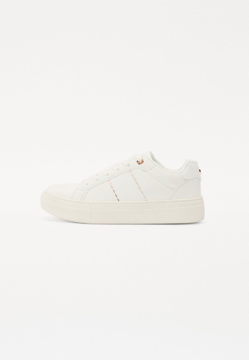 Fehér sneaker sima bőrből készült felsőrésszel, két varrott csíkkal, lekerekített orral és bézs gumi talppal. Rózsaarany fűzőlyukakkal díszített.