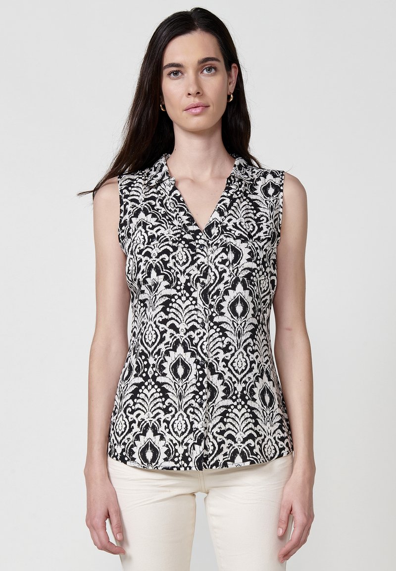 Blusa senza maniche con un motivo floreale bianco e nero, dotata di colletto, chiusura con bottoni e tessuto dalla consistenza liscia.