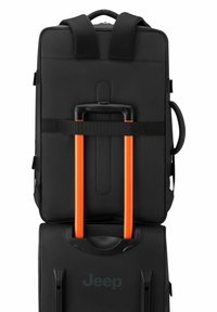 Mochila negra con correas ergonómicas, un mango retráctil naranja y un logo en una superficie suave, diseñada para viajar y ofrecer comodidad.