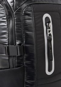 Detailní záběr na černý zip tašky s tažítkem s logem, plastovou přezkou a texturovaným lesklým panelem látky.