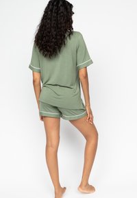 Zielony zestaw z krótkim rękawem i pasującymi szortami, wykonany z miękkiej tkaniny z białymi wykończeniami. Luźny krój i nieco dłuższy tył.