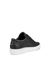 Sneaker en cuir noir avec surface texturée, design sans lacets et sangles élastiques. Semelle en caoutchouc blanc avec un subtil accent beige au talon.