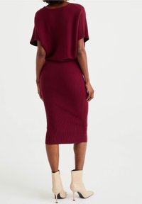 Burgunderfarbendes, geripptes Strickkleid mit lockerem Oberteil und taillierter Rockpartie. Getragen mit beigen Ankle Boots mit spitzer Zehenpartie und hohen Stiletto-Absätzen.