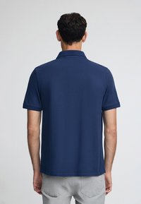 Marinblå pikétröja med korta ärmar, platt krage och lätt textur. Har sömmar längs kragen och ärmsluten.