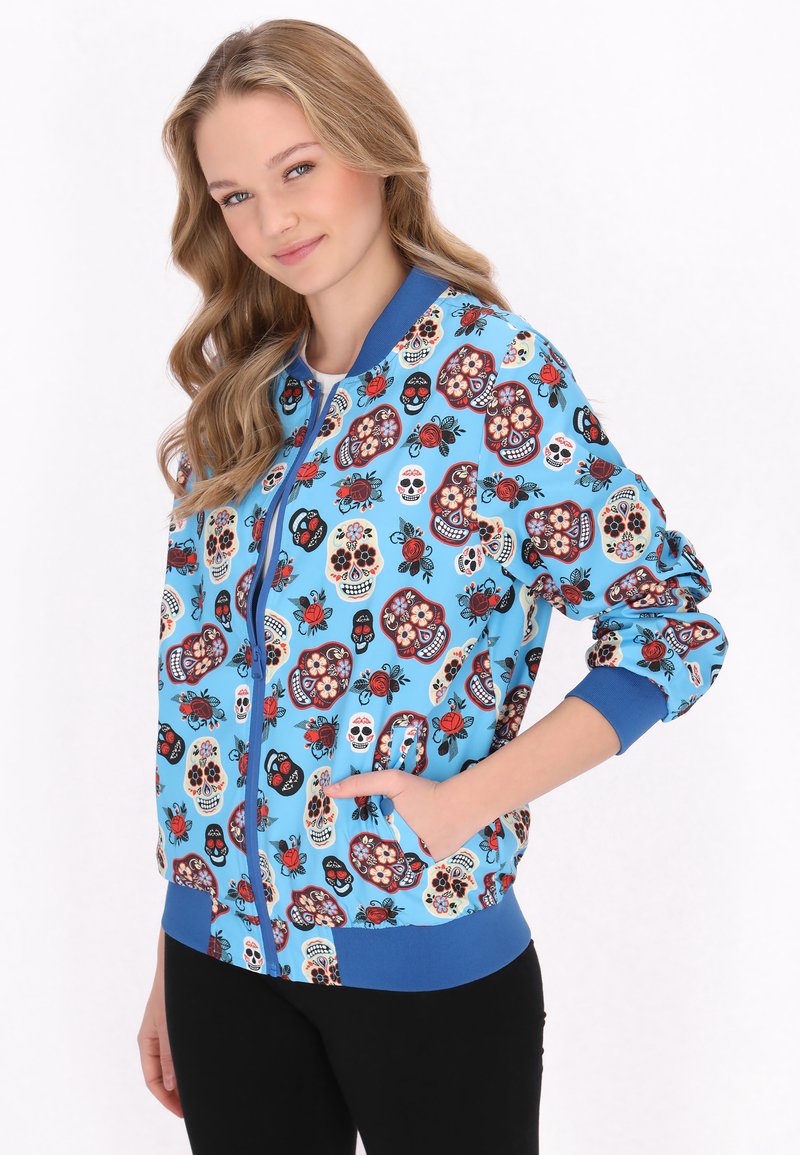Jachetă bomber albastră cu un model colorat de skull și accente florale. Are fermoar în față și manșete și tiv elastic. Două buzunare laterale.