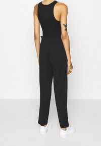Top negro sin mangas con escote redondo combinado con pantalones negros de cintura alta. El conjunto presenta una textura suave y una silueta ajustada.