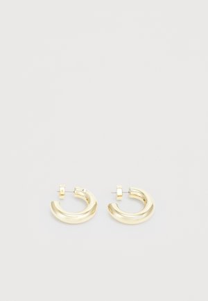Boucles d'oreilles en forme de créoles en ton or, avec une finition lisse et polie. Présentent un design courbé et un petit accent près de la tige pour un détail supplémentaire.