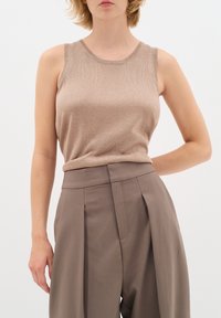Top senza maniche beige realizzato in un tessuto strutturato, abbinato a pantaloni taupe a vita alta con pieghe, creando un look a strati.