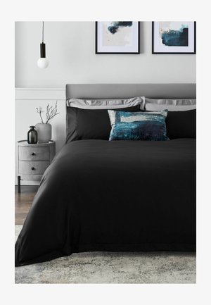 Kingsize-Bett mit schwarzer Bettwäsche, grauem gepolstertem Kopfteil, blauem Zierkissen, rundem grauem Nachttisch, Hängeleuchte und zwei abstrakten Wandbildern.