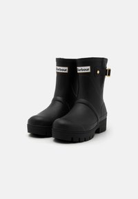 Black rubber ankle boots with a textured surface, round toe, rugged sole, and gold-accented buckle detail. Features Barbour branding.