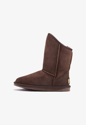 Hnědé semišové kotníkové boty s kulatou špičkou, odhaleným ovčím kožichem, kontrastním prošíváním a plochou gumovou podrážkou. Logo na vnější straně.