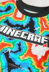 Buntes Minecraft-Themen-Shirt mit einem pixelierten Muster in Blau, Orange, Grün und Rot. Verfügt über einen schwarzen gerippten Kragen und ein auffälliges Logo.