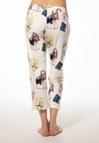 Vrouw die blootsvoets staat, gekleed in een korte crèmekleurige broek met een kleurrijke tas en kledingprints.