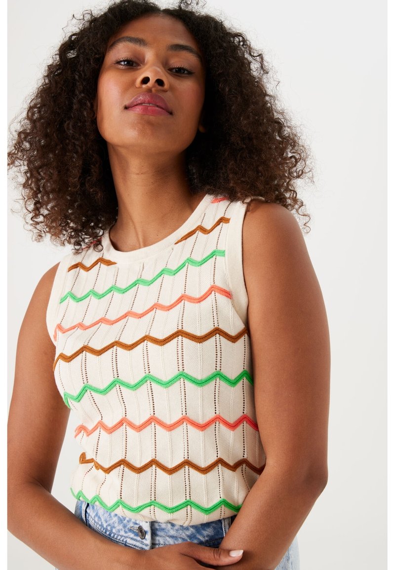 Mouwloze gebreide top in crème met zigzagpatronen in groen, oranje en bruin. Beschikt over een ronde halslijn en een gestructureerde stof.