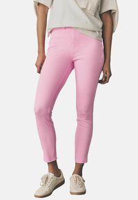 Jeans rosas ajustados de algodón elástico, con un diseño clásico de cinco bolsillos y una textura suave, combinados con zapatillas beige.