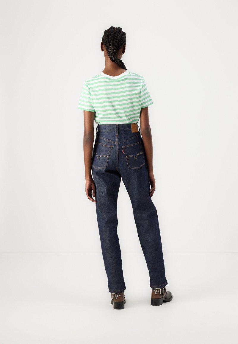 Camiseta a rayas verde y blanca con cuello redondo, combinada con jeans de mezclilla oscuros de tiro alto, que cuentan con bolsillos traseros y una etiqueta de cuero color tostado.