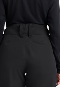 Zwarte high-waisted broek heeft een gladde textuur en een strakke uitstraling, met verstelbare lussen in de taille en minimale merkidentificatie.