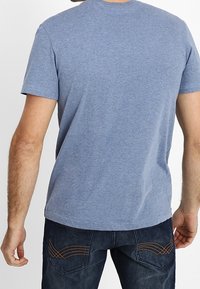 Blue short-sleeve t-shirt with a crew neck, made from a soft fabric. Features a smooth texture and a straight hem. Worn with dark jeans.