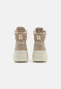 Beige hoge sneakers met een gestructureerde suède afwerking, robuuste witte rubberen zool en opvallende FILA-branding aan de achterkant.