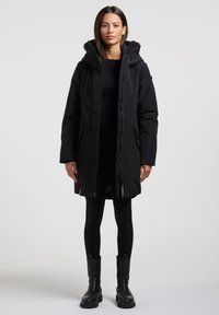 Sort parka med hætte, med lynlåslukning foran, sidelommer og justerbare snore. Lavet af et glat, vejrbestandigt stof.