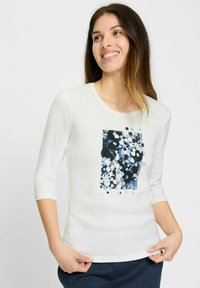 Witte blouse met lange mouwen met een grafisch ontwerp van blauwe en zwarte stippen op een rechthoekig patroon. Zachte textuur met een getailleerde vorm.