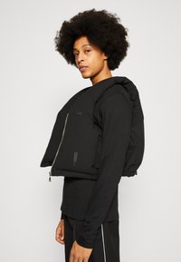 Casaco puffer preto com colarinho alto, mangas oversized e fecho à frente. Apresenta uma textura suave e detalhes de marca discretos.