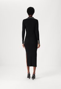 Svart ribbat stickat klänning med långa ärmar, sidoklyftor och pärlaccents vid ärmsluten och kragen. Buren med svarta högklackade skor.