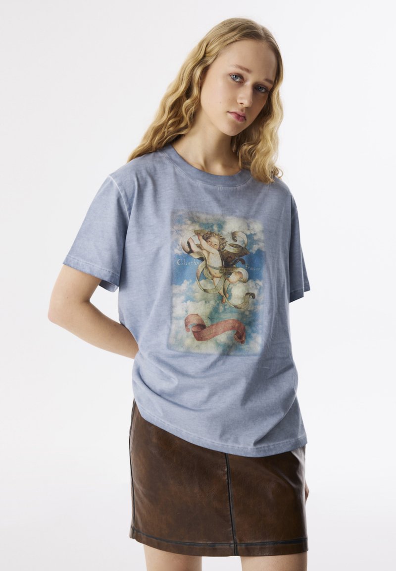 Camiseta de algodón azul claro con un gráfico vintage que presenta nubes y una cinta. Combinada con una mini falda de cuero marrón oscuro.