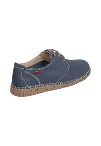 Zapato casual azul marino con suela moteada beige, cordones marrones, costuras blancas y tacón bajo, visto de lado.
